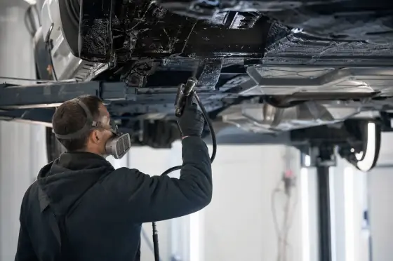 Мастер наносит антикоррозийное покрытие на днище автомобиля